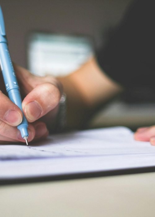 Close-up of hand writing in notebook using a blue pen, focus on creativity.